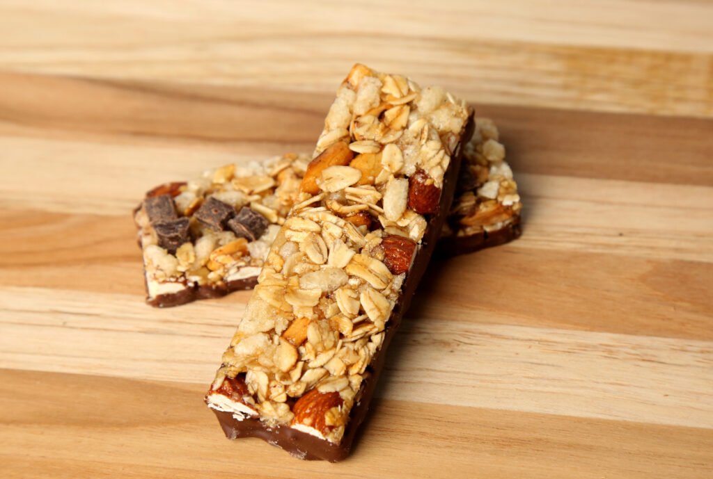 Assortment of the top 10 recommended emergency foods laid out on a table Energy / protein bars made with chocolate and nuts placed on a wooden surface.